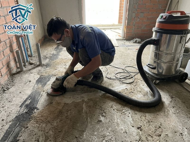 Thợ mài phẳng và hút sạch bụi trên mặt sàn bê tông trước khi dán màng