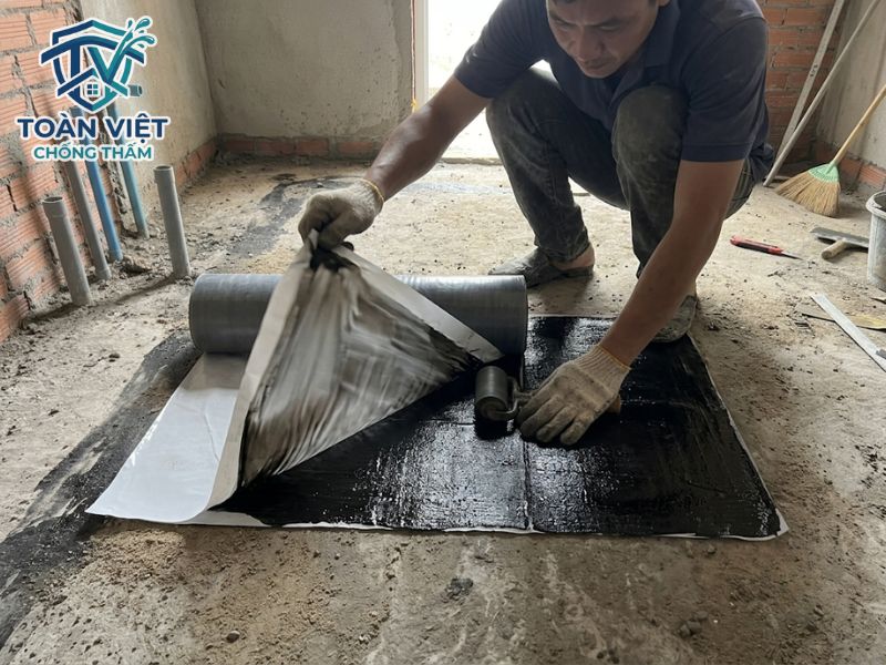 Thợ vừa bóc lớp màng nilon bảo vệ keo vừa trải màng, tay kia dùng con lăn miết chặt vị trí mép nối chồng lên nhau
